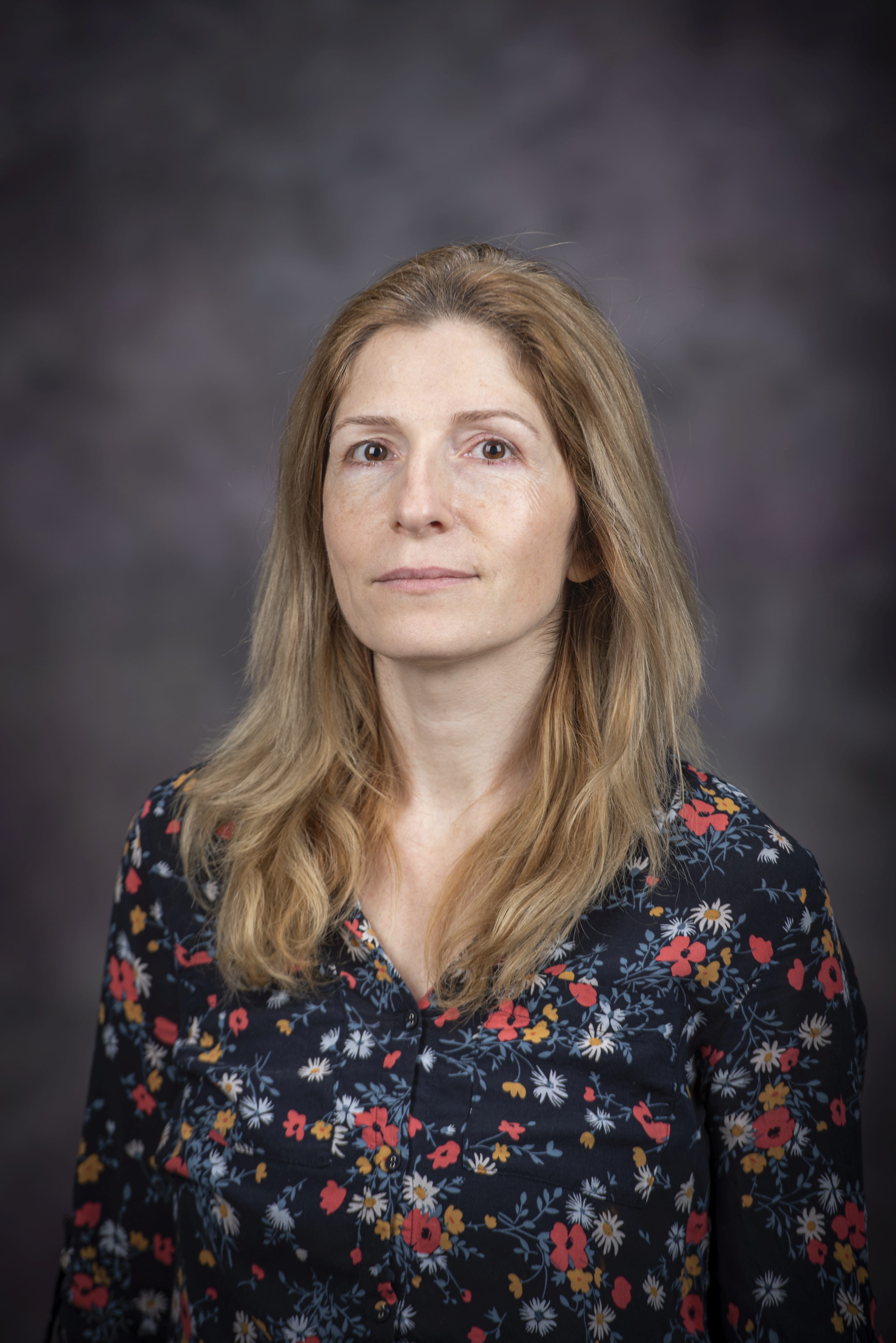 Woman with light brown hair smiling, wearing a dark blue floral print top