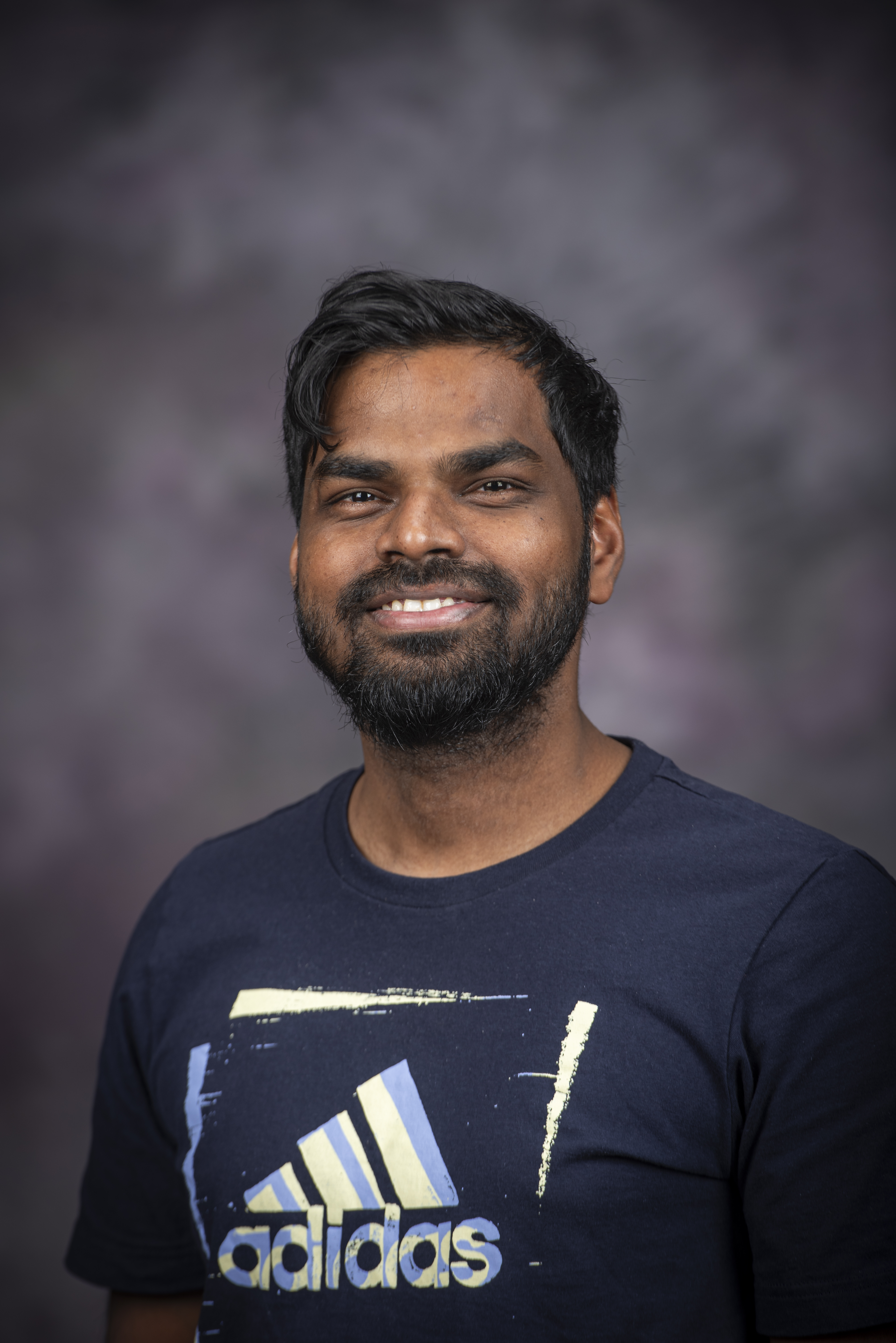 Man with dark hair, moustache and beard smiling with navy t-shirt