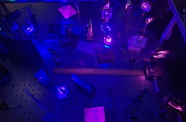 Picture of the setup with the lights off. While it may look cool, the prism’s glow is not particularly helpful when aiming for a clean spectrum (see Fig. 2). Between the prisms, the beam path is made visible in the air. 